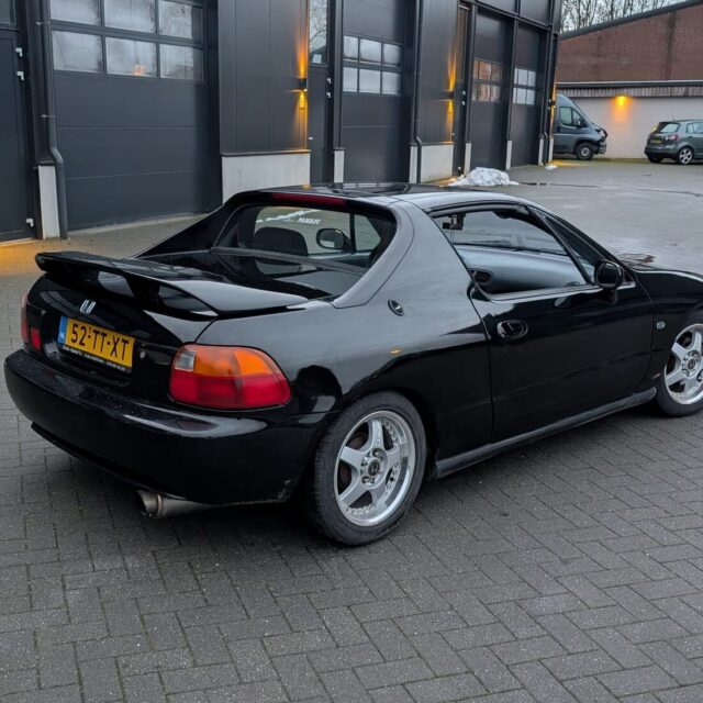Zwarte Honda CRX Del Sol coupé met spoiler en zilveren velgen geparkeerd op een klinkerterrein